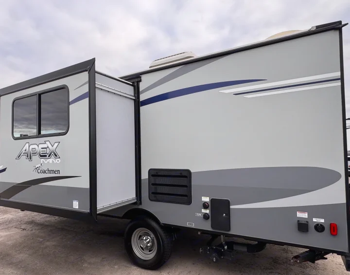 Side view of a light gray Apex Nano Coachmen RV rental, featuring an open pop-out, window, and utility hookups.. Coachmen Apex Nano 2022