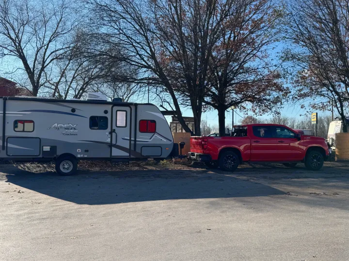 Red Chevy Silverado towing an Apex Nano RV rental under a clear sky with bare trees.. Coachmen Apex Nano 2022