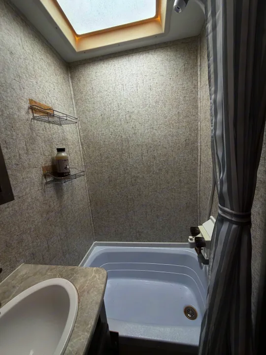 Inside an RV rental bathroom: a compact tub/shower with a skylight, sink, and useful wall shelves for toiletries.. Coachmen Apex Nano 2022
