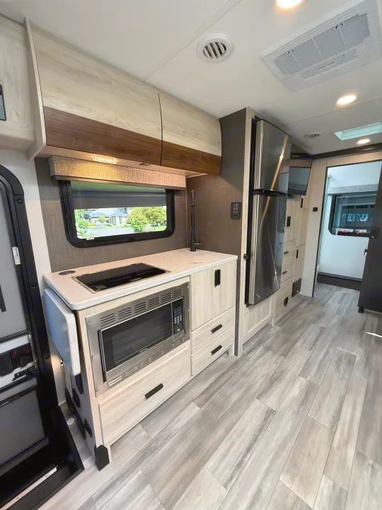 RV rental kitchen: light wood-grain cabinetry, countertop, sink, stovetop, microwave, and full-size refrigerator.. Forest River Sunseeker MBS 2022