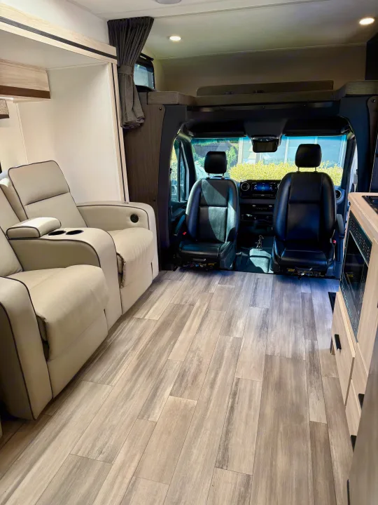 Modern RV rental interior showcasing cream recliners, wood-look flooring, and the front cockpit with black seats.. Forest River Sunseeker MBS 2022
