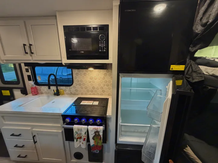 This RV rental kitchen features an open EverChill fridge, High Pointe microwave, stovetop, and sink with a hexagonal backsplash.. Jayco Jay Flight Baja Edition 2024