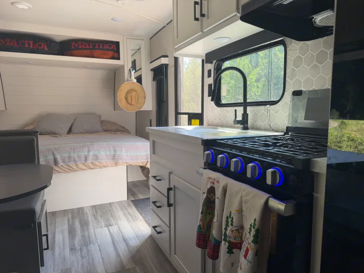 Cozy rv rental interior featuring a modern kitchen with blue-lit stove, sink, and honeycomb backsplash, next to a comfy bed.. Jayco Jay Flight Baja Edition 2024
