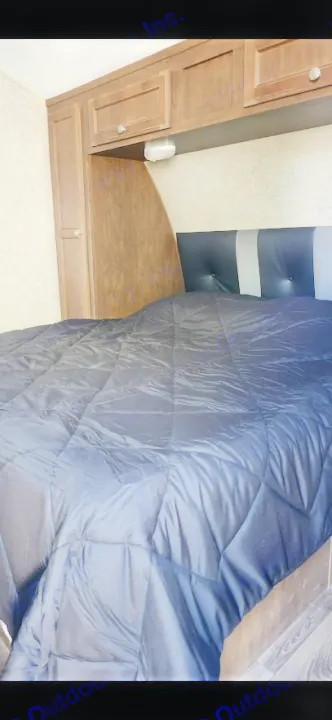 Cozy RV rental bedroom with dark comforter, striped headboard, and wooden cabinets. Perfect for your next adventure.. Sonic Sonic Trailer 2019