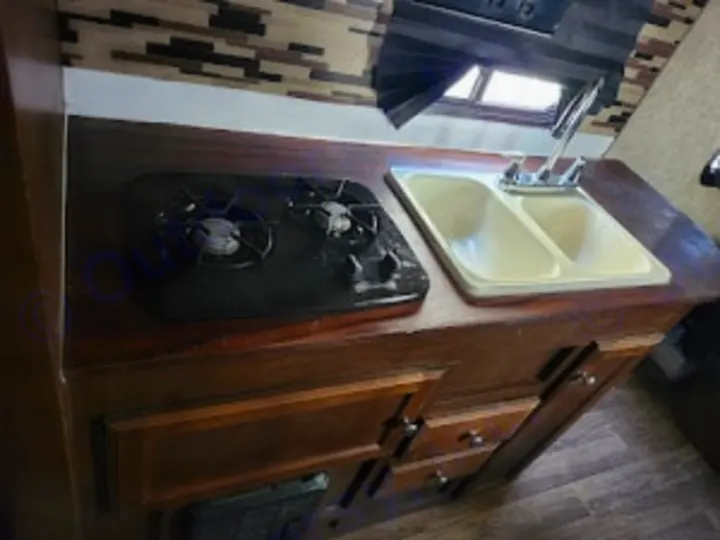 Compact RV rental kitchen with a two-burner stove, double sink, and wooden cabinets. Perfect for camper cooking.. Sonic Sonic Trailer 2019