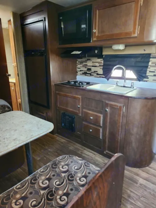 RV rental kitchen and dining area with fridge, microwave, stove, sink, and patterned bench seating.. Sonic Sonic Trailer 2019