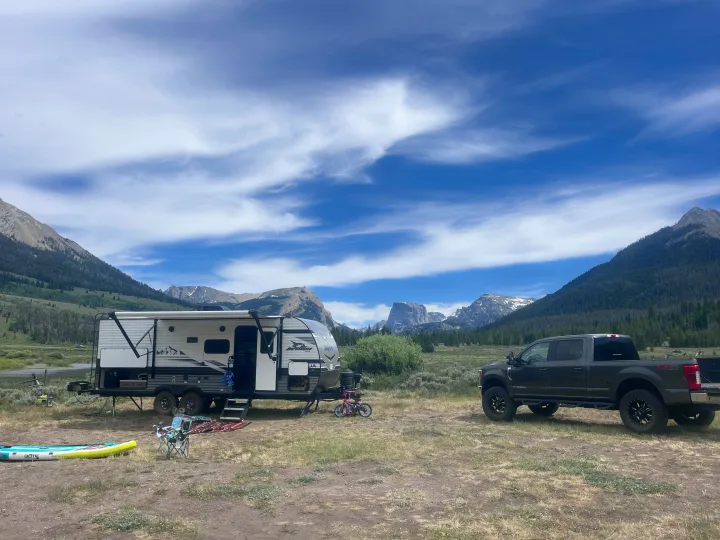 An rv rental (travel trailer) and truck are parked for camping in a scenic mountain valley under a blue, cloudy sky.. Jayco Jay Flight Baja Edition 2024