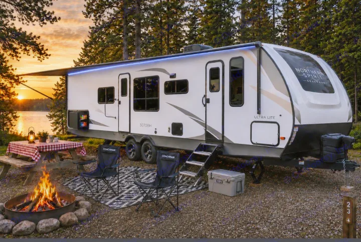 Serene RV rental campsite: travel trailer by a lake at sunset, featuring campfire, picnic table & chairs.. Forest River Coachmen Northern Spirit Ultra Lite 2026