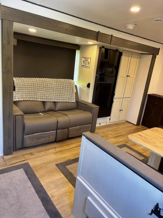 Comfortable RV rental living space features a gray recliner sofa, dining area, and kitchen access, enhanced by wood accents.. Forest River Coachmen Northern Spirit Ultra Lite 2026