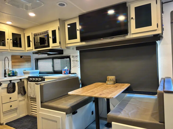 Modern RV rental interior: a compact kitchen, dinette with light wood table & grey benches, and a large TV. Ready for adventures!. Forest River Coachmen Northern Spirit Ultra Lite 2026