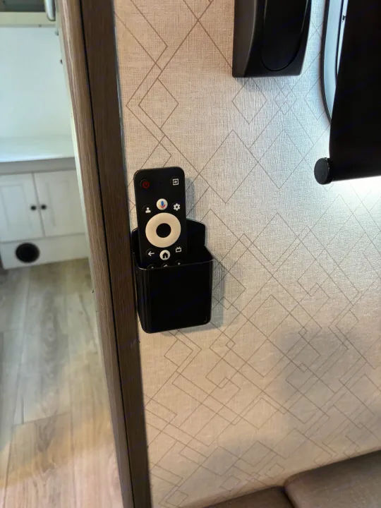 Stay organized in your RV rental: a smart TV remote neatly secured in a wall-mounted holder on a patterned wall.. Forest River Coachmen Northern Spirit Ultra Lite 2026