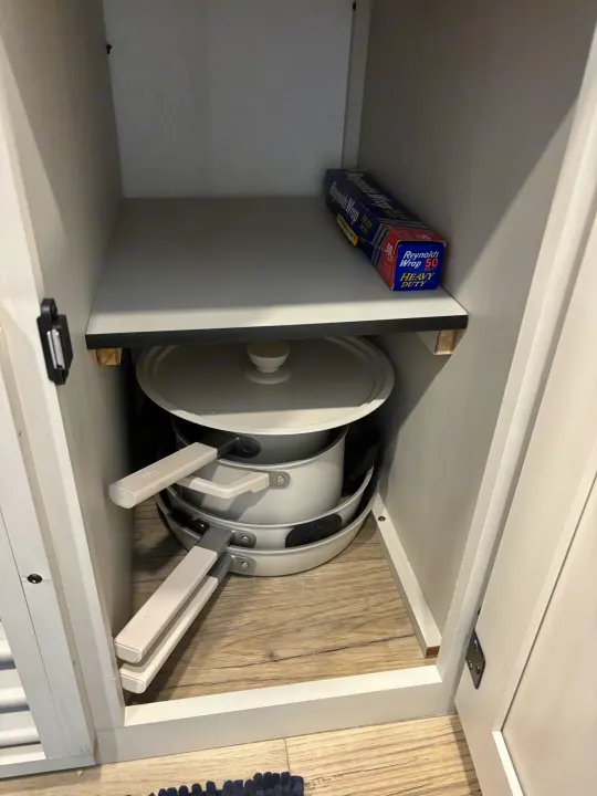 RV rental cabinet: stacked gray pots/pans below a shelf with heavy-duty aluminum foil, neatly organized.. Forest River Coachmen Northern Spirit Ultra Lite 2026