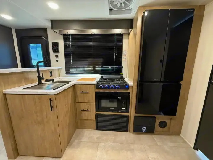 Modern RV rental kitchen featuring light wood cabinets, black sink, stovetop, microwave, and large refrigerator.. Forest River Campsite Reserve 2026