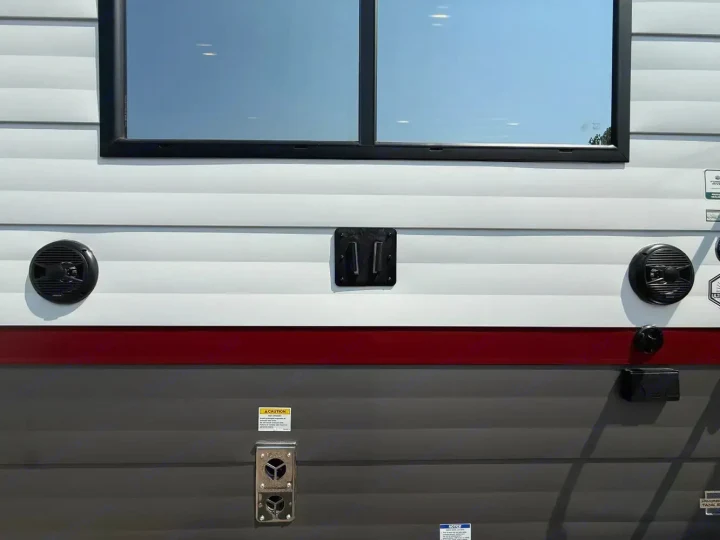 Side view of an RV rental showing its window, exterior speakers, and furnace vent. Common RV hookups are also visible.. Forest River Campsite Reserve 2026