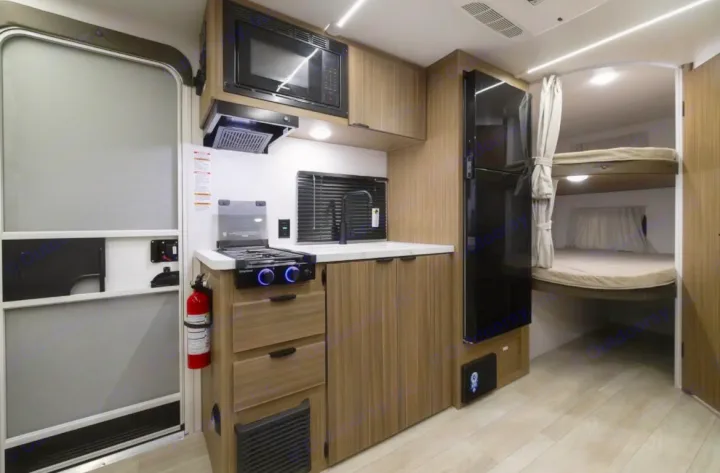 Compact rv rental interior showing a small kitchen with stove, microwave, fridge, and bunk beds in the back.. Forest River Salem FSX 2025