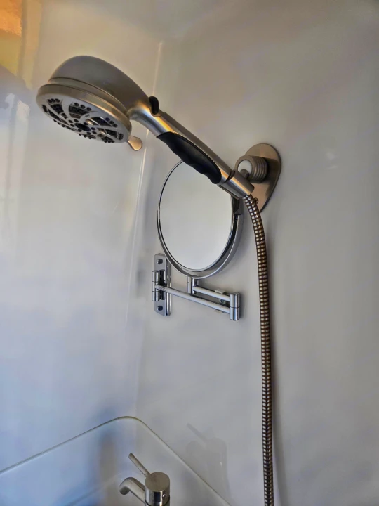 Compact RV rental bathroom featuring a modern handheld shower, adjustable magnifying mirror, and sleek faucet.. Coachmen Galleria 2023