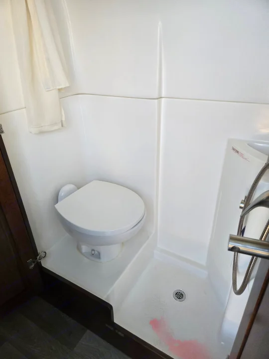 Compact RV rental bathroom features a white toilet and integrated shower with a visible reddish stain on the floor.. Coachmen Galleria 2023