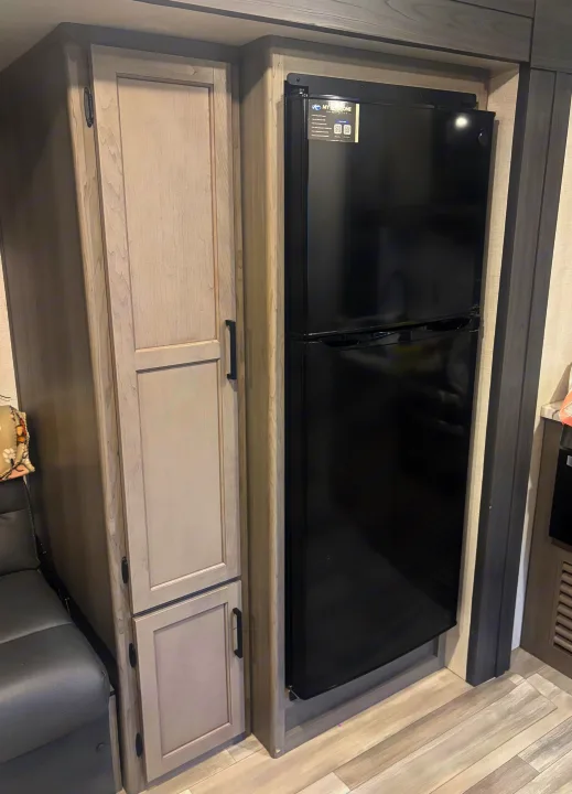 Inside an RV rental: a black refrigerator, light-colored storage cabinets, and gray seating area are visible.. Keystone RV Hideout 2024