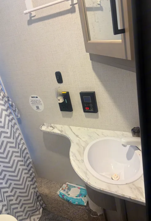 Inside an RV rental: a compact bathroom with a sink, water heater panel, outlet, and a chevron shower curtain.. Keystone RV Hideout 2024
