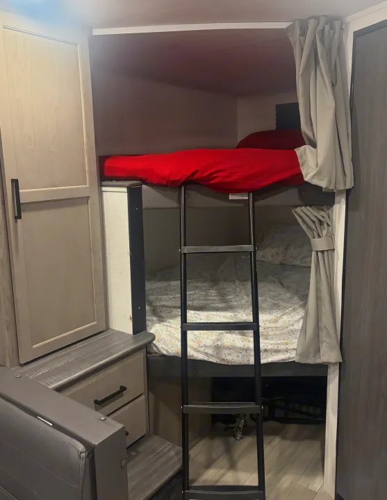 RV rental bunk beds with ladder, privacy curtains, and adjacent storage. Ideal for compact sleeping area.. Keystone RV Hideout 2024