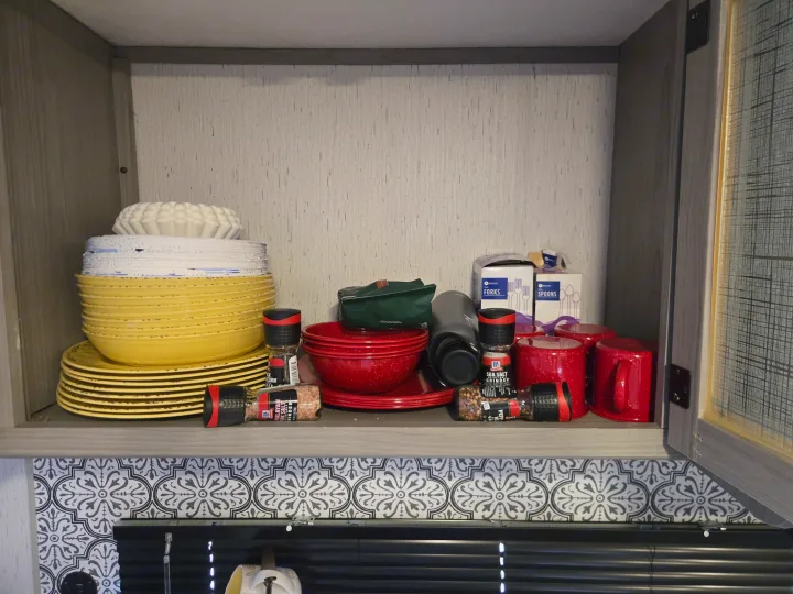An rv rental kitchen cabinet filled with neatly stacked yellow & red dishes, mugs, and essential spices.. Dutchmen Coleman Lantern 2022