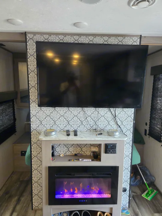 Stylish RV rental entertainment center with TV, patterned wall, and electric fireplace for a cozy living space.. Dutchmen Coleman Lantern 2022