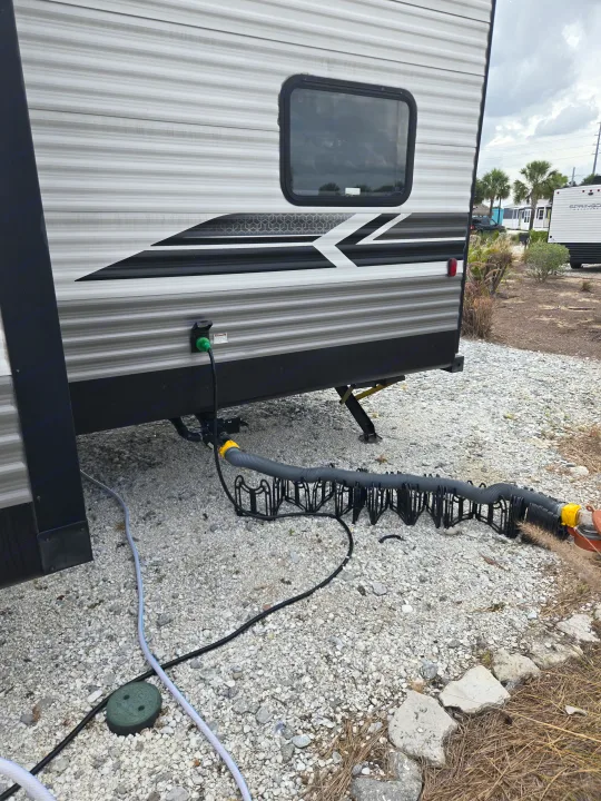 RV rental showing power, sewer, and water hookups on a gravel campsite. This travel trailer is fully connected.. Dutchmen Coleman Lantern 2022