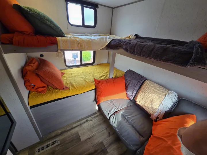 Cozy RV rental interior featuring vibrant bunk beds with colorful blankets & pillows, plus a comfy seating area.. Dutchmen Coleman Lantern 2022