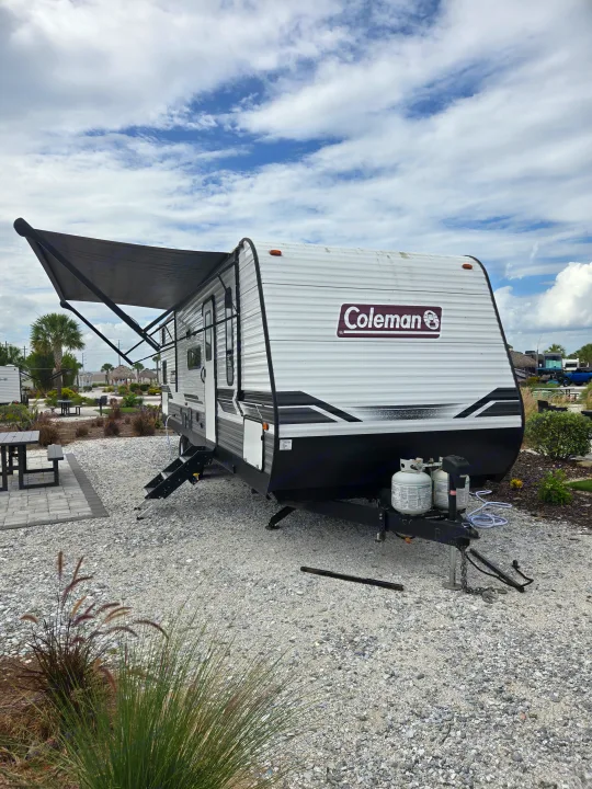 Enjoy a Coleman travel trailer RV rental set up with an awning and picnic table at a scenic gravel campsite under a cloudy sky.. Dutchmen Coleman Lantern 2022