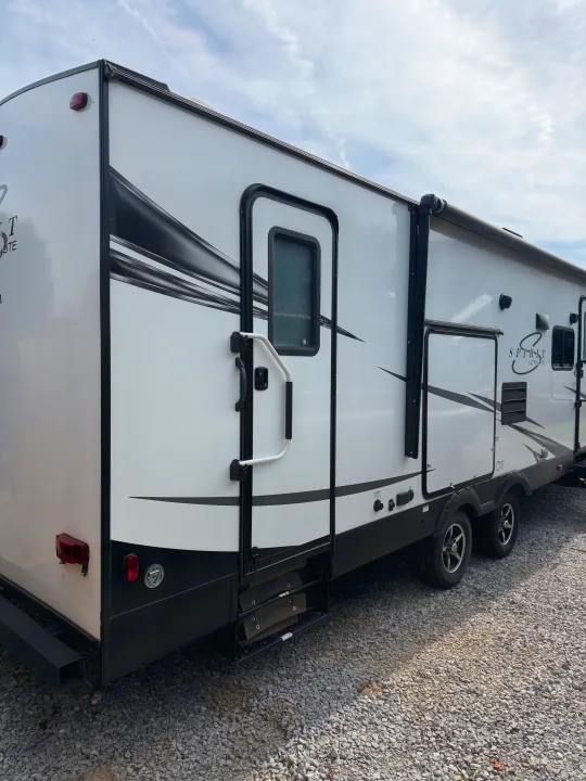 Side view of a white and black Spirit Ultralite travel trailer on a gravel lot, ready for your next RV rental.. Coachmen Spirit Lite Ultra 2963BH 2020