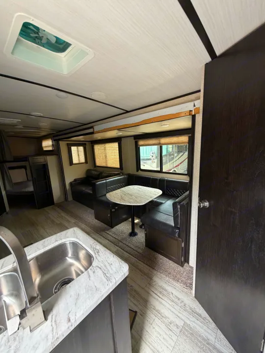 Modern RV rental interior: kitchen sink, dining booth, dark leather seating, bunk beds, and wood-look floors.. Coachmen Spirit Lite Ultra 2963BH 2020