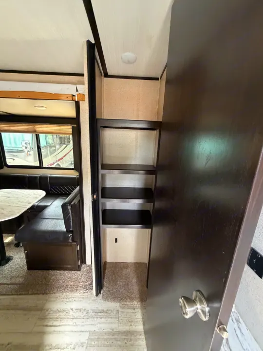 RV rental interior showing a dinette with bench seating & table, alongside a pantry/closet with shelving & a dark door.. Coachmen Spirit Lite Ultra 2963BH 2020