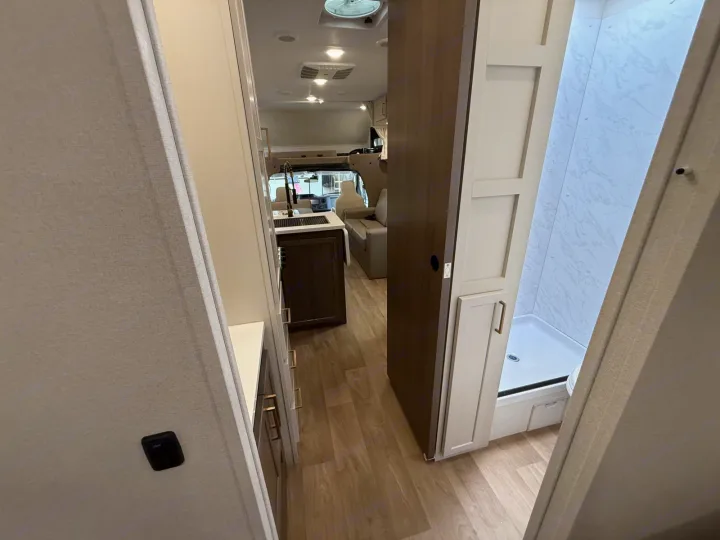 Inside this RV rental: view down a narrow aisle to a compact kitchen, living area, and a functional bathroom with shower.. 2027