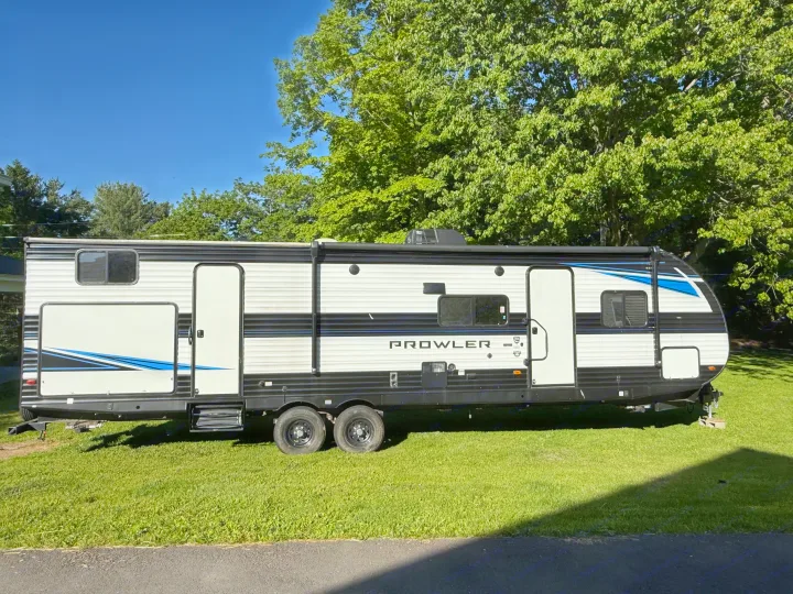 This Prowler RV rental is ready for your next camping adventure, parked on green grass under a clear blue sky.. Heartland RVs Prowler 2022