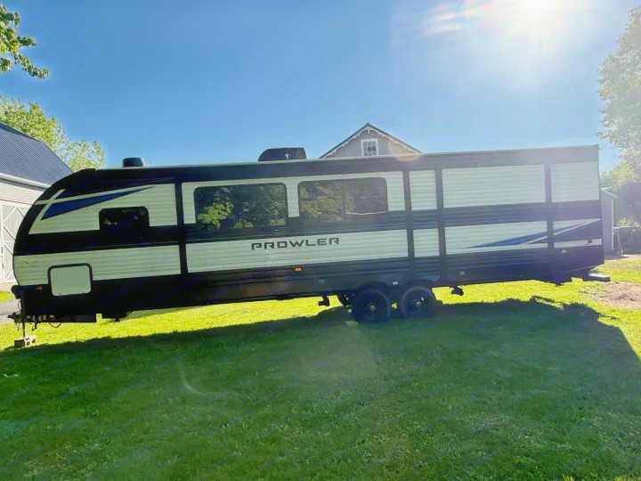 This Prowler travel trailer, ideal for an rv rental, is parked on a sunny green lawn with a house in the background.. Heartland RVs Prowler 2022