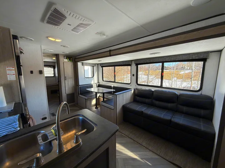 Spacious RV rental interior features a kitchen sink, dinette, sofa, and bright windows with outdoor views.. Heartland RVs Prowler 2022