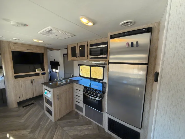 Modern rv rental kitchen & living area with stainless steel appliances, light wood cabinets, and TV.. Heartland RVs Prowler 2022
