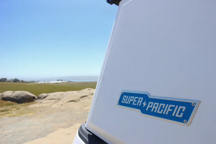 Super Pacific rv rental camper side with its logo, overlooking a scenic landscape of rocks, grass, water, and blue sky.. Ford Ford F150 2017