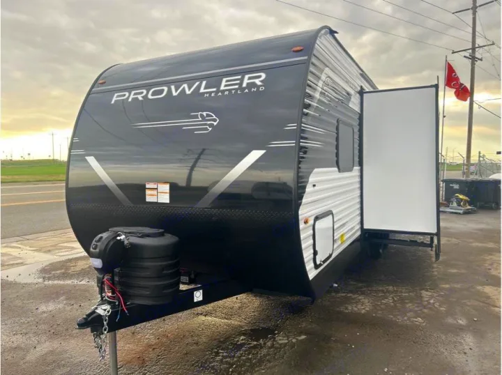 Black and white Prowler Heartland travel trailer, door open, parked on a wet lot. Explore with this RV rental for camping adventures.. Heartland Powler 2026