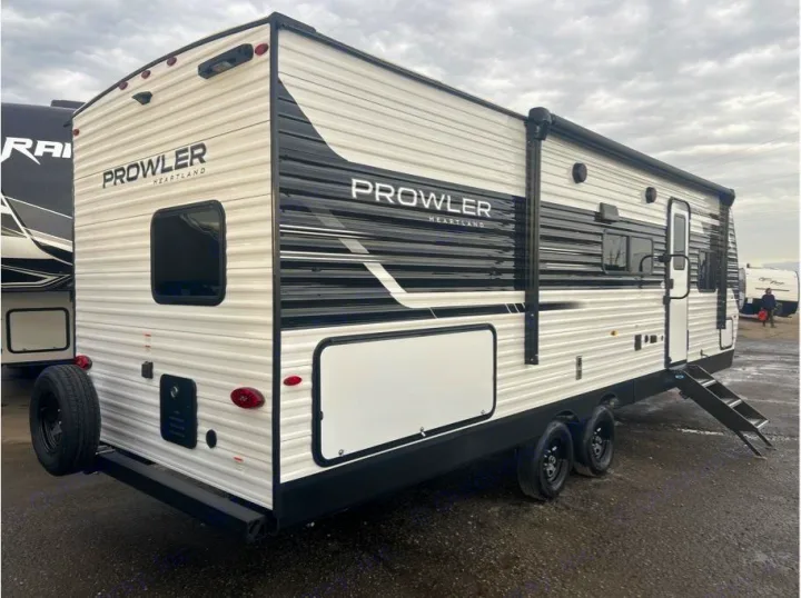 This modern Prowler Heartland travel trailer, perfect for an RV rental, features a white exterior with black graphics, awning, and rear spare tire.. Heartland Powler 2026