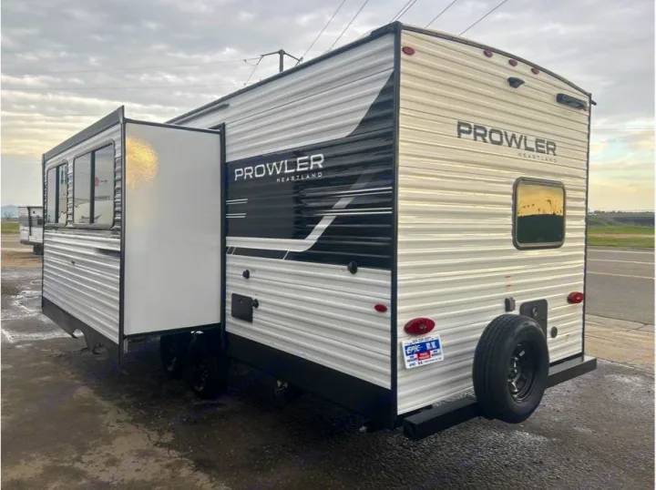 This Prowler Heartland travel trailer, ideal for RV rental, features a white and black exterior with an extended slide-out and rear spare tire.. Heartland Powler 2026