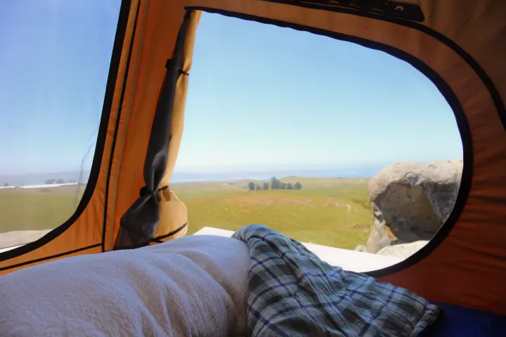 Serene ocean views from a comfortable rooftop tent setup, perfect for your next RV rental road trip. Bed and blanket visible.. Ford Ford F150 2017