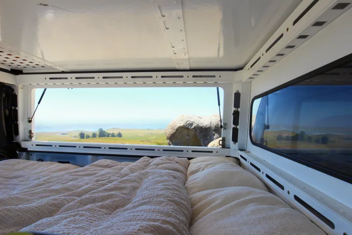 Cozy bed inside an RV rental offering scenic views of coastal hills & ocean. Ideal for camping adventures!. Ford Ford F150 2017