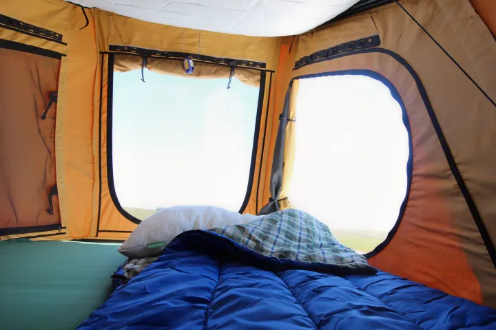 Cozy RV rental tent interior: green sleeping pad, blue sleeping bag, pillow, and a bright outdoor view through two windows.. Ford Ford F150 2017