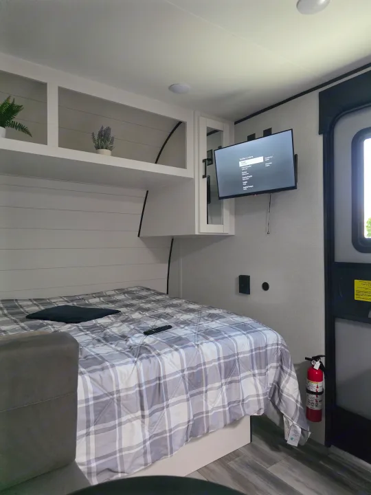 Modern RV rental bedroom: comfy plaid bedding, a wall-mounted TV, overhead storage, and an accessible fire extinguisher.. Jayco Jayco 2026