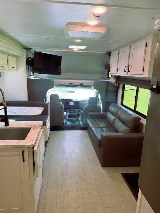 Bright RV rental interior featuring a kitchen, dinette, sofa, and front cab with an overhead bunk bed.. East to West Entrada 2023