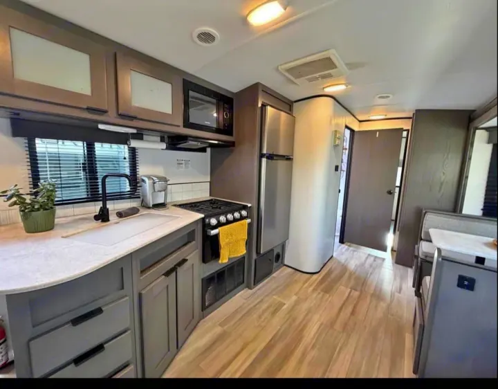 Explore this modern RV rental featuring a full kitchen with microwave, stove, sink, and refrigerator, alongside a compact dining area.. Cruiser RV MPG Ultra Lite 2021