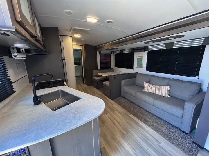 This clean RV rental boasts a modern kitchen, cozy gray sofa, and dinette, offering a welcoming interior for your adventures.. Cruiser RV MPG Ultra Lite 2021
