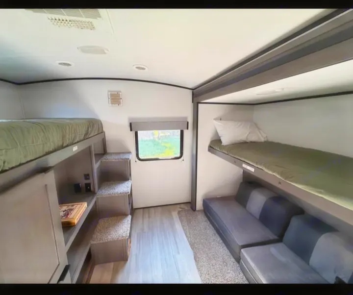An RV rental bunkroom with olive green bunk beds, a comfortable gray sofa, and integrated storage steps for access.. Cruiser RV MPG Ultra Lite 2021