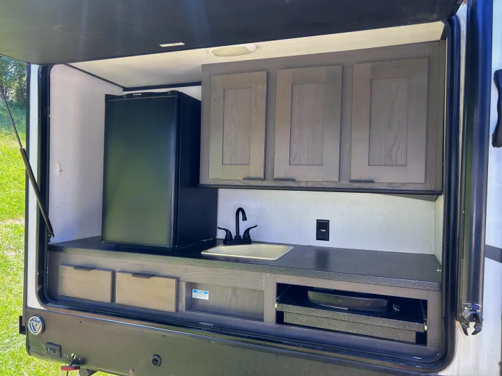 This RV rental outdoor kitchen features a fridge, sink, cabinets, and a pull-out cooktop for convenient outdoor cooking.. Cruiser RV MPG Ultra Lite 2021